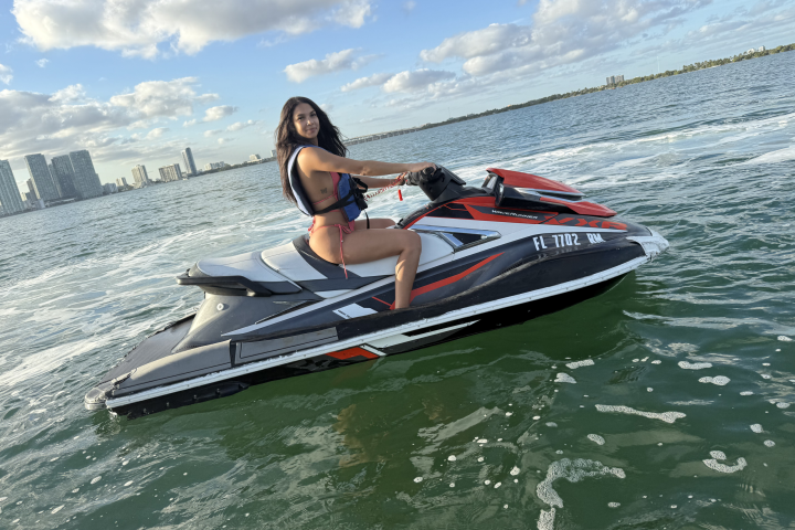 Person on a jet ski in sunny waters with city skyline in the background.