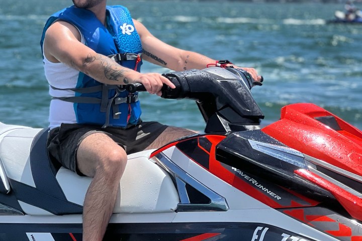 Person in blue life jacket riding a red and black jet ski on the water.